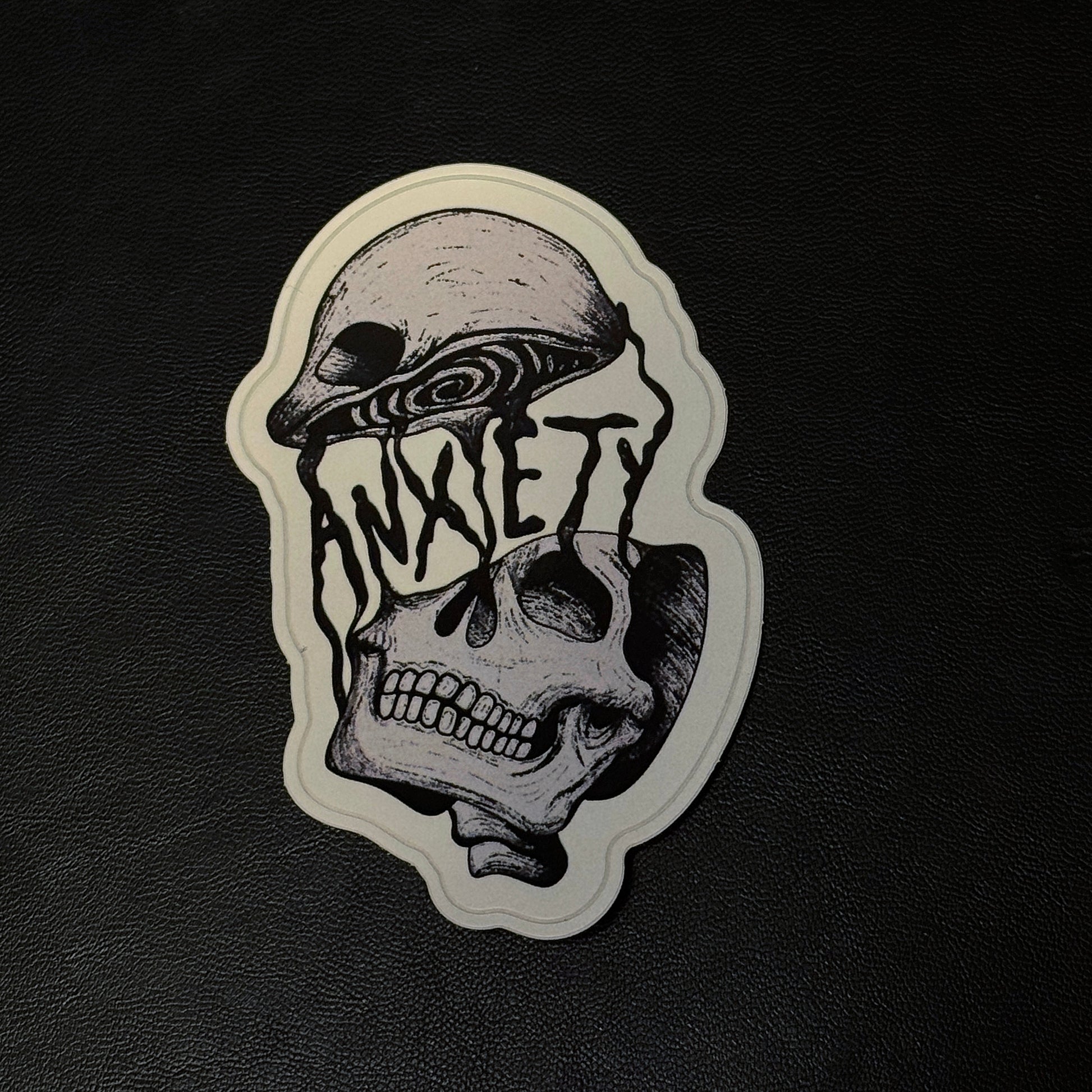 A die-cut vinyl sticker featuring a black and white illustration of a skull with the word 'ANXIETY' integrated into the face, shown on a textured black background.